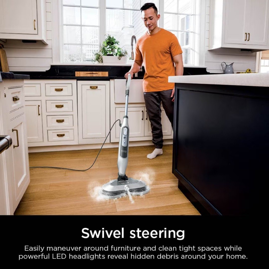 Man steam mopping a hardwood kitchen floor with the Shark Steam & Scrub, showing swivel steering and LED headlights